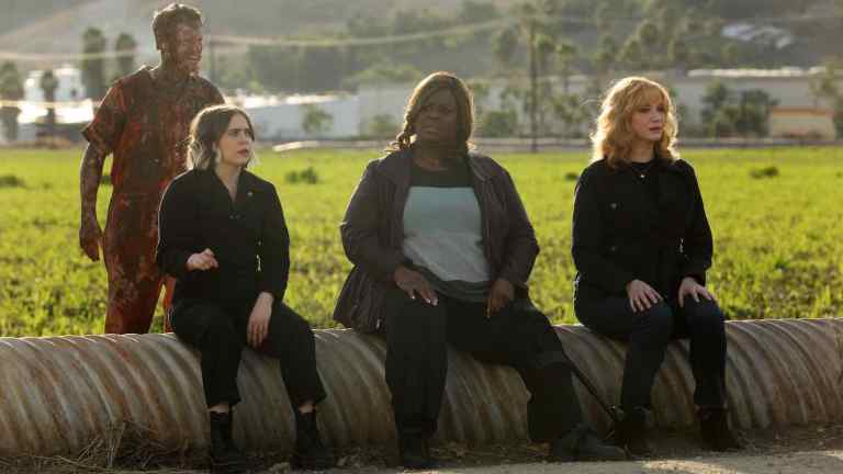 The three stars of Good Girls sit on a pipe in front of a field