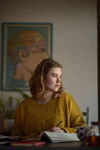 Author Caroline Hardaker sits at a desk, looking away from the camera with a pen in her hand