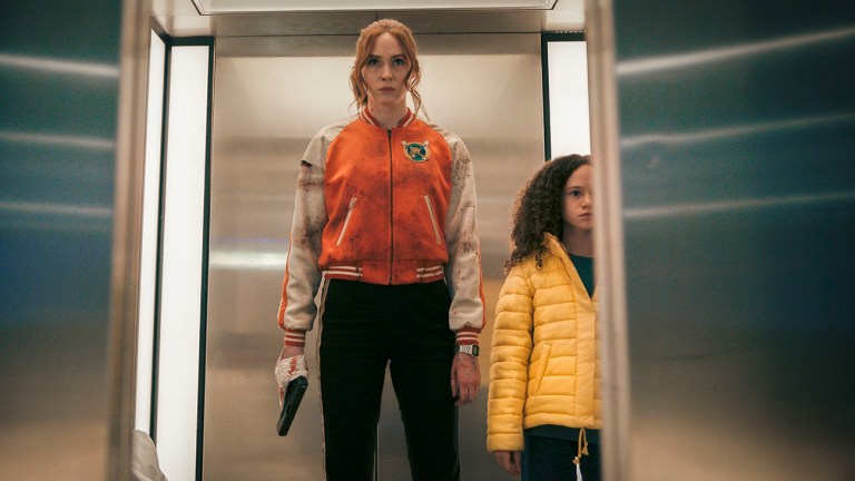 Karen Gillan as Sam stands in an elevator with a gun taped to her hand in Gunpowder Milkshake