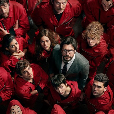 The cast of Money Heist look up in a crowd of people in red