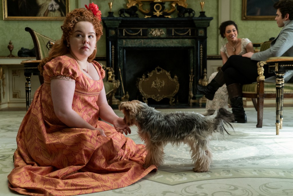NICOLA COUGHLAN as PENELOPE FEATHERINGTON plays with a dog on the floor in Bridgerton Season 2