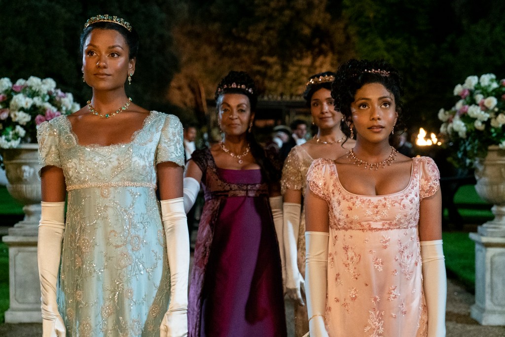 Simone Ashley as Kate Sharma, Adjoa Andoh as Lady Danbury, Shelley Conn as Mary Sharma enter an outdoor party in fancy dresses in Bridgerton