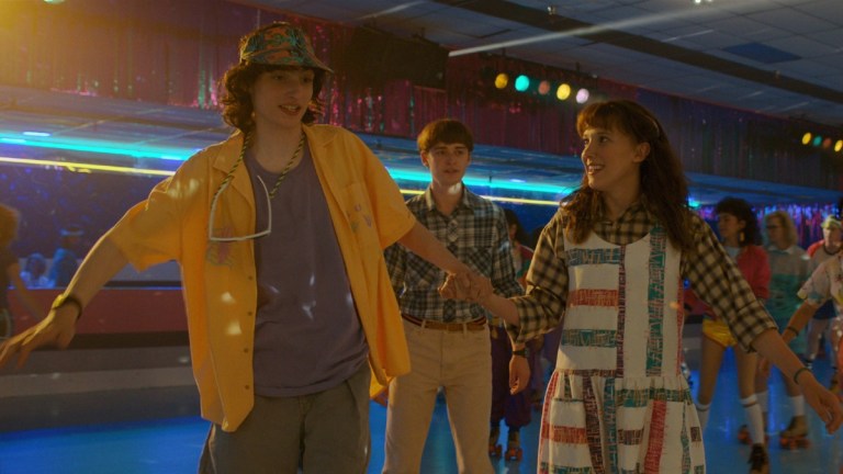 Mike Wheeler (Finn Wolfhard), Will Byers (Noah Schnapp), and Eleven (Millie Bobby Brown) at a roller rink in Stranger Things season 4
