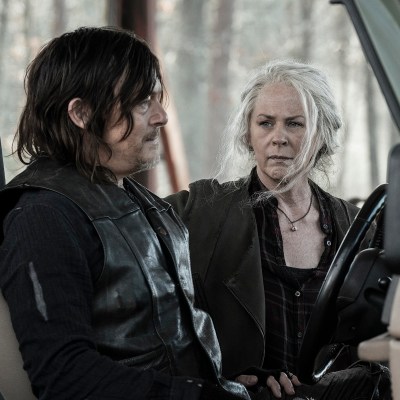 Norman Reedus as Daryl Dixon sits behind the wheel of a jeep while Melissa McBride as Carol looks on concerned.