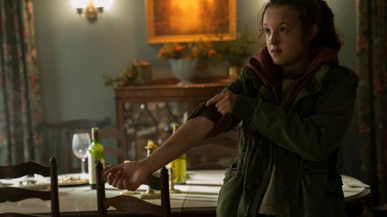 Bella Ramsey as Ellie in HBO's The Last of Us standing in a dining room holding out her bitten arm