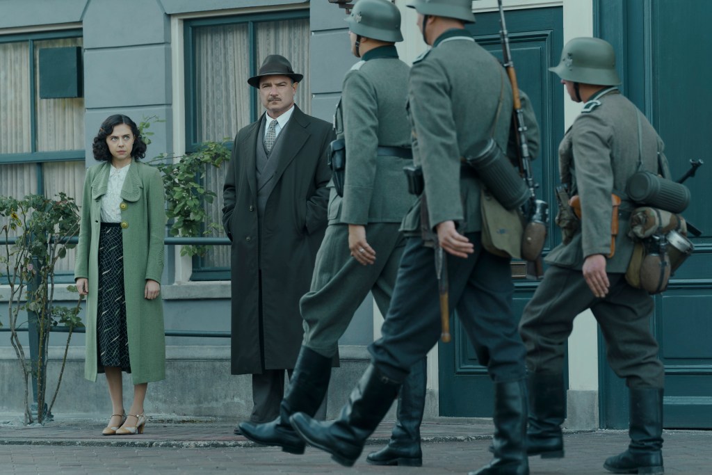 Miep Gies, played by Bel Powley, and Otto Frank, played by Liev Schreiber, watch as Nazi soldiers march down the street in Amsterdam. (Photo credit: National Geographic for Disney/Dusan Martincek)