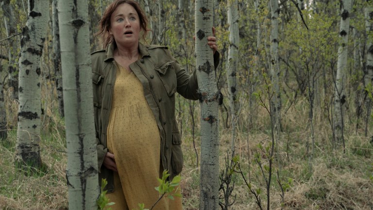 Anna Williams (Ashley Johnson) stands pregnant, in a yellow dress and green jacket in The Last of Us