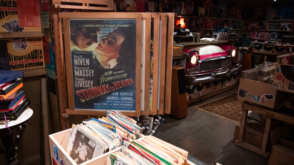 Good Omens season 2 set photo - Maggie's Record Shop poster rack. Credit: Prime Video