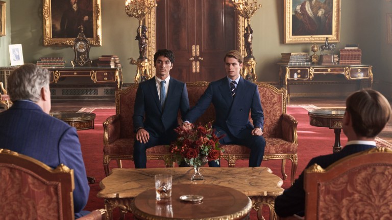 Nicholas Galitzine as Prince Henry and Taylor Zakhar Perez as Alex Claremont-Diaz hold hands while sitting in a royal palace