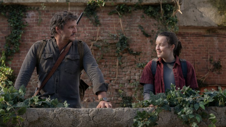 Joel (Pedro Pascal) and Ellie (Bella Ramsey) stand smiling at each other in HBO's the Last of Us