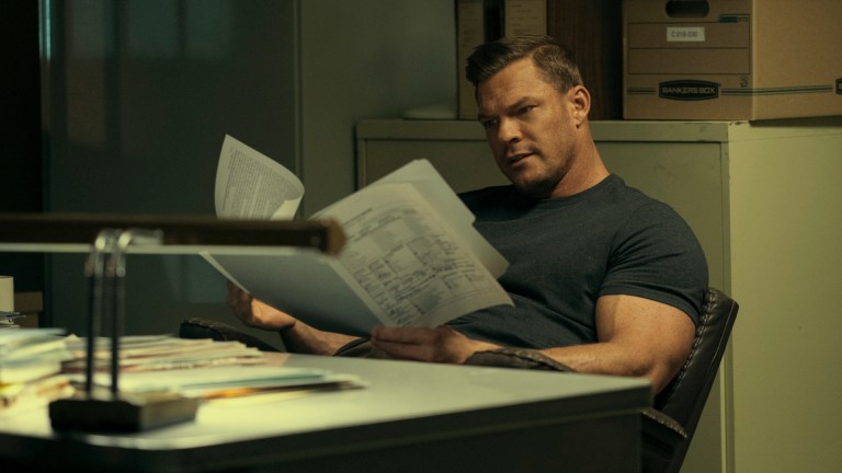 Jack Reacher (Alan Ritchson) sits at a desk combing through files in Prime Video's Reacher