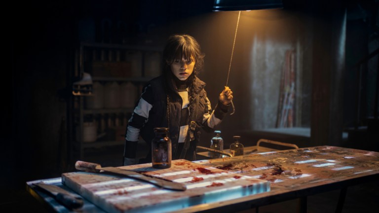 Wednesday Addams (Jenna Ortega) stands in front of a creepy, bloody work table in episode 106 of Wednesday