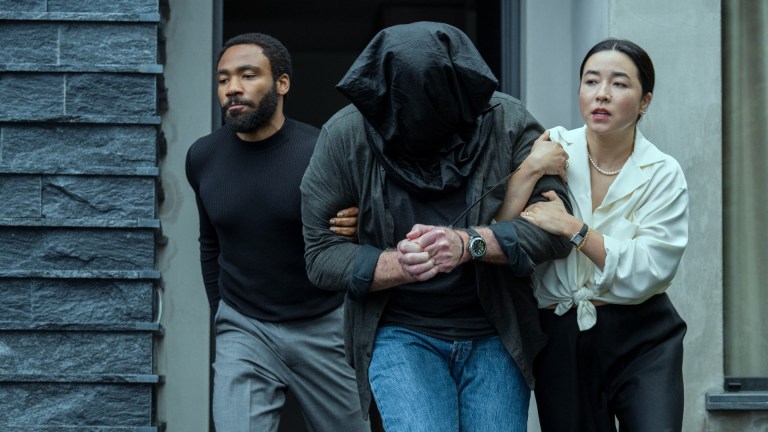 Donald Glover and Maya Erskine guide a man with a black bag over his head in Mr. and Mrs. Smith.