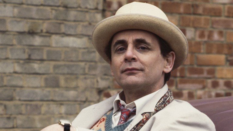 Sylvester McCoy in costume in a white suit and hat with an umbrella as the Seventh Doctor in Doctor Who