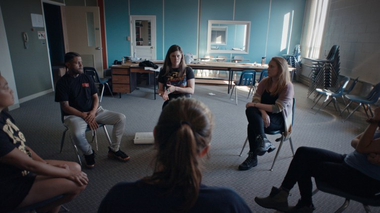A still from Netflix documentary The Program featuring several adults sitting on chairs in an abandoned classroom.