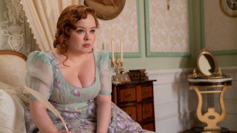 Nicola Coughlan as Penelope Featherington, sitting on her bed with a quill in hand in episode 306 of Bridgerton