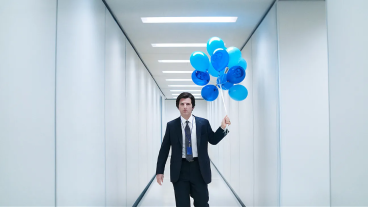 Mark S of Severance carrying blue baloons in hallway.