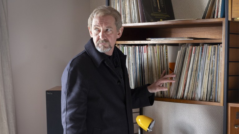 Ian Hart standing next to a shelf of vinyl records in Shetland series 9