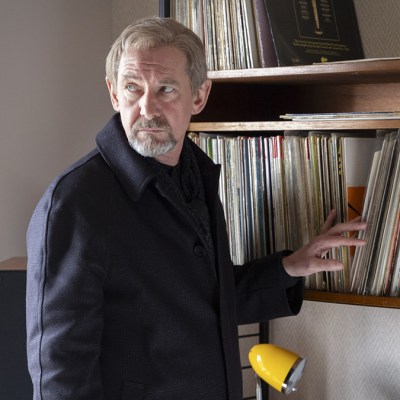 Ian Hart standing next to a shelf of vinyl records in Shetland series 9