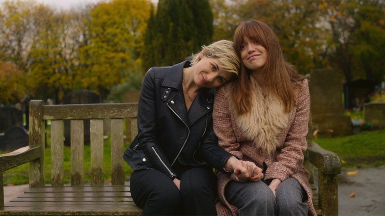Jodie Whittaker and Aimee-Lou Wood sitting on a park bench smiling