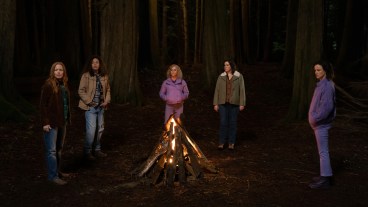 Lauren Ambrose as Van, Tawny Cypress as Taissa, Christina Ricci as Misty, Melanie Lynskey as Shauna and Juliette Lewis as Natalie stand around a campfire in the wilderness in YELLOWJACKETS, "Storytelling".