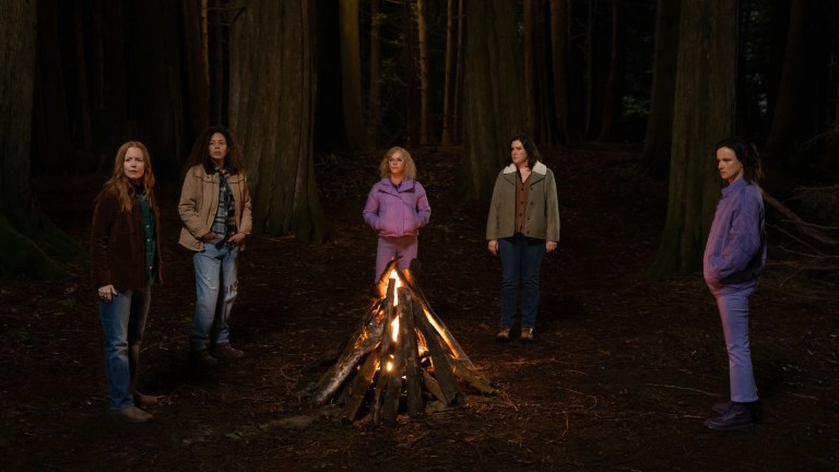Lauren Ambrose as Van, Tawny Cypress as Taissa, Christina Ricci as Misty, Melanie Lynskey as Shauna and Juliette Lewis as Natalie stand around a campfire in the wilderness in YELLOWJACKETS, "Storytelling".
