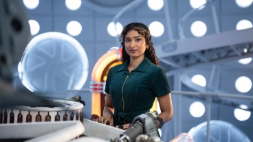 A woman in a green jumpsuit standing by the TARDIS console in Doctor Who