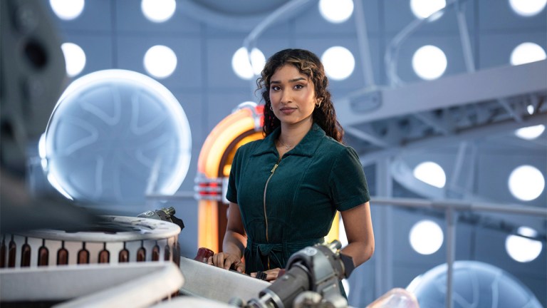 A woman in a green jumpsuit standing by the TARDIS console in Doctor Who