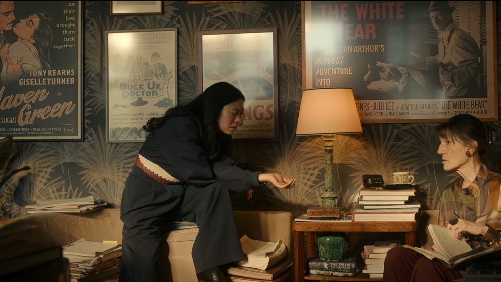 Awkwafina in front of a wall of framed fake movie posters including Haven Green and White Bear in Black Mirror episode Hotel Reverie