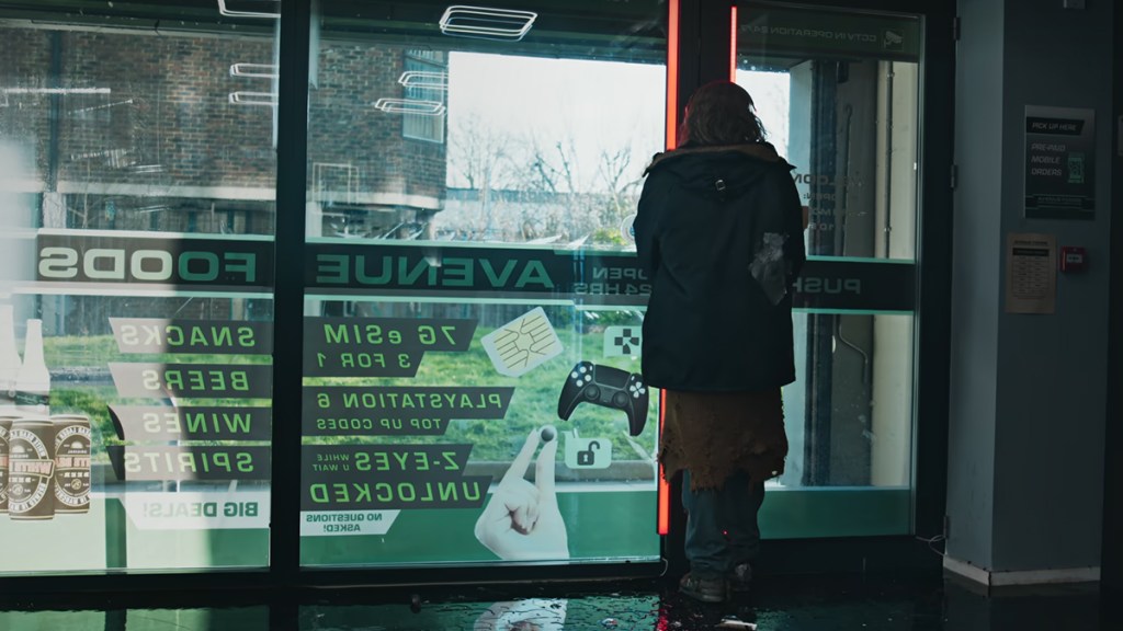 A scruffy man seen from behind against a shop window with adverts in it