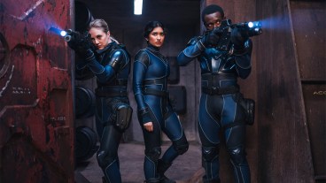 Three people in spacesuits holding guns on a mining base in space