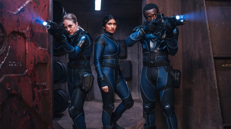 Three people in spacesuits holding guns on a mining base in space