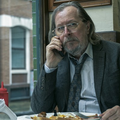 Gary Oldman in a dirty suit and tie on his mobile phone and eating a full English breakfast as Jackson Lamb in Slow Horses