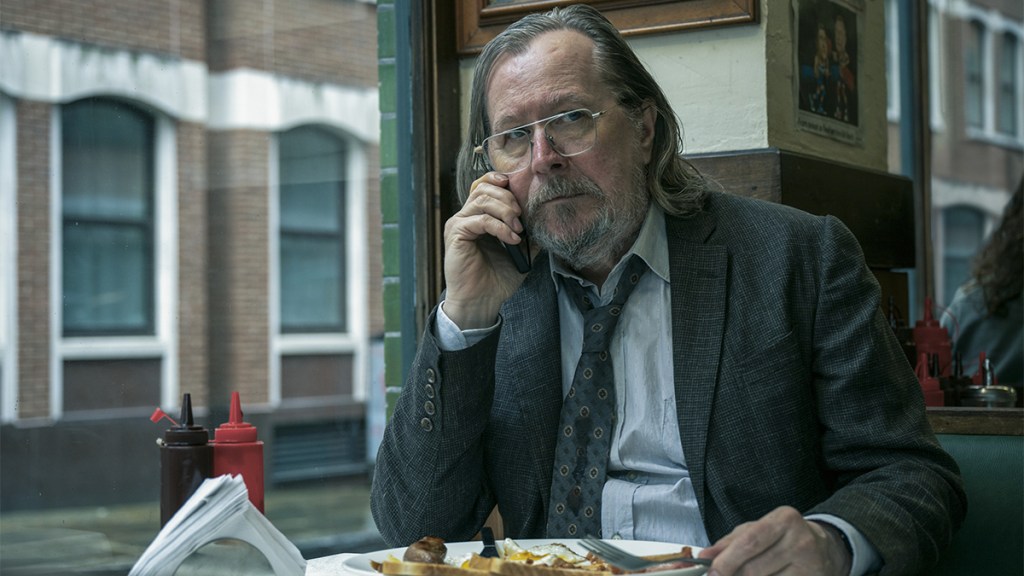 Gary Oldman in a dirty suit and tie on his mobile phone and eating a full English breakfast as Jackson Lamb in Slow Horses