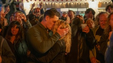 Peacemaker (John Cena) kisses Harcourt (Jennifer Holland) at the Foxy Shazam concert in Peacemaker season 2.