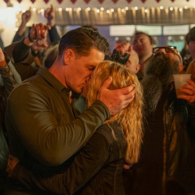 Peacemaker (John Cena) kisses Harcourt (Jennifer Holland) at the Foxy Shazam concert in Peacemaker season 2.