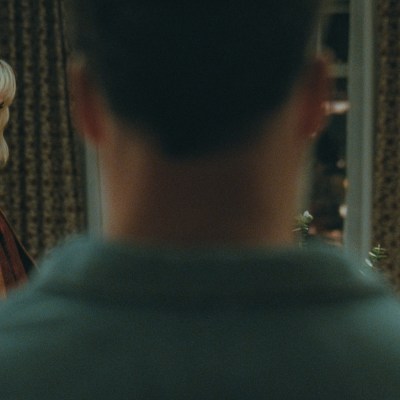 I’m not going to begin by stating emphatically that Penelope Cruz and Edward Norton play sexy-time ghosts in Olivia Wilde’s The Invite… but what if they might be ghosts, who happen to be sexy? I’m joking, but also stay with me for a minute. Still high off its buzzy premiere at Sundance, The Invite walks, blurs, and utterly dissolves all manner of boundaries and bougie festival taboos. Floating with an ethereal mystique that borders on the occult, as well as a painfully hilarious naturalism, this is a movie that orbits around a marriage in midlife catastrophe to the point of dizziness—an even more impressive feat after the film was marketed with such deceptive seduction. To be sure, Cruz and Norton are quite appealing, the seemingly perfect couple upstairs in a posh, if ancient, New York City tenement building. They initiate friendly conversation in the elevator, look gorgeous while making preternatural eye contact with neighbors, and apparently have passionate, earth-shattering sex after midnight each evening. Angela and Joe (Wilde and Seth Rogen) should know. They hear it every night through their ceiling, along with a 12-year-old daughter who is never seen in the film. There is something just otherworldly about Piña and Hawk (Cruz and Norton). And it leaves our central couple so alternatingly resentful and envious that the movie begins with an insert card of an Oscar Wilde quote: the eternal harbinger of doom for any romantic sentimentality beyond skin-deep nihilism. So when Joe and Angela invite Piña and Hawk over for a couple’s dinner, something aloof is in the air. Joe thinks it’s tension, as he is more than ready, eager even, to complain about the animal sounds through the floorboards. But for our spirited guests, the tension could have an entirely different flavor, one of suspense as they are here to—eventually—propose the downstairs stuffed shirts join them in a shared sexual experience. They want to swing by switching spouses for the night. The ghostly element I mentioned earlier is a bit of a come-on, but not by much. While the film quotes Wilde, Oscar, there’s more than a touch of Dickens and his descendants about the way Piña and Hawk float into our unhappy protagonists’ lives. They’re kinky Jacob Marleys, freaky Clarences, the angel of mercy in It’s a Wonderful Life who’s come to grant Jimmy Stewart a second chance at life after decades of disappointment by getting frisky in the kitchen. Even the audience is tempted into thinking they’re watching one kind of beguiling sex comedy, which we kind of get, even as we’re really being lured into a far more existential exploration of love and marriage after the romance has died. Are things not already in the Twilight Zone when an orgy invite from strangers amounts to the closest thing to high romance Joe or Angela’s heard in years? The trick of Olivia Wilde’s film and its inviting screenplay by Rashida Jones and Will McCormack is its structure. Based on the Spanish film The People Upstairs, Wilde’s picture borrows the original’s real-time setting of an unwieldy night of collapsing inhibitions and glasses of wine giving way to low-lit confessions in a cozy apartment’s corners. Among Jones and McCormack’s many scripted innovations, however, is the sensation that this is occurring in a bit of a theater workshop. This isn’t a knock at the performances, which are excellent, but at the sense we are sitting with a group of professionals, also over wine, as they psychoanalyze and deconstruct a messy, impermanent thing: the marriage of two people who care for each other but lost love a long time ago. Wilde shoots the film almost wholly in steadicam and in an underlit setting wherein the decorative paint colors and apartment accoutrements that Angela distracts herself with are indistinguishable. She isn’t wrong to note Joe is checked out when she talks about “finishing” the bedroom several years on, but Wilde the filmmaker cannot let her character hide behind minutiae. She drowns Angela and Joe’s faux domesticity into an inviting yet gloomy shadow world. Similarly, the helmer constantly films Rogen’s Joe as a domineering force in the life of his wife, towering over the frame and shot in harsh low light like a Halloween fright mask. At other times, the pair are caught in line of sight of each other in their horseshoe-shaped apartment, with the duo able to simply look up across the way and see one another in parallel windows. Yet they never do. It would make eye contact and break the spell of mutually agreed upon isolation. At its core, though, one does not cast a talent like Rogen, or for that matter Wilde at her most mischievous, and not revel in the humor. Rogen accentuates a new note of tired resignation to his likable, schlubby everyman persona, but there’s a lot more bitterness to Joe than Matt Remick in The Studio, as well as more pathos. This is a sad sack too self-involved to recognize he’s dragging his marriage down, but his unhappiness is not unsympathetic to anyone who reached a certain point in life where they realized they did not become the person they dreamed about when they were 20. It also makes his acerbic digs at Piña and Hawk, particularly for the latter’s clearly self-chosen name, all the more biting. Meanwhile Cruz delights in her role that purposefully walks a line between the ethereal and earthy. For much of the film, she might be a cipher, or certainly a projection of Joe and even Angela’s desires, albeit in very different contexts, but Cruz plays it with a rueful self-awareness. She’s the cat plucking at a pair of wounded canaries’ wings. The scene where she specifically attempts to uncoil Joe out of his wound-up funk to Sade’s now 26-year-old(!) “By Your Side” is a harmonious car crash; a collision of sweetness and cringe, reverie and gallows humor despair. And I haven’t even mentioned his “dance” moves. The Invite is a shimmering dramedy for adults of a certain age, and perhaps a sobering epiphany that this can now be so acutely tailored to elder Millennials and younger Gen-Xers at that. The film is genuinely sexy but in the awkward and disarming way of clumsy foreplay. It stumbles and stammers, with its proverbial pants caught around the ankles before the whole thing tonally keels over. Yet for all the screenplay’s verbose intellectualization about sensuality, and Wilde’s obvious preoccupation with it as a storyteller, the main event is something more intimate and unspoken. It’s a lament about the passage of time, milestones left discarded, and maybe even marriages that also have outlived their shelflife. One might even call it haunting, complete with the mysterious good-looking specters descending from above. Penelope Cruz and Olivia Wilde in The Invite Review