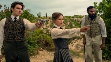 "Three people in vintage clothing stand outdoors in a rugged, green landscape; two point pistols ahead while the third stands beside them with a cane, all looking alert and tense." Enola Holmes 3. (L to R) Louis Partridge as Tewkesbury, Millie Bobby Brown as Enola Holmes and Himesh Patel as Dr. Watson in Enola Holmes 3. Cr. John Wilson/Netflix ©2026